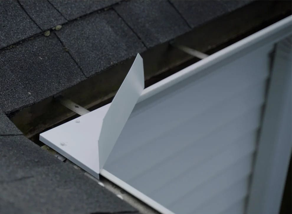 Close-up of a metal flashing installed along the edge of a shingled roof, showing the junction between the roof and a vertical siding wall. Close-up of a metal flashing installed along the edge of a shingled roof, showing the junction between the roof and a vertical siding wall.