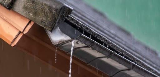 Rainwater is leaking from a clogged gutter on the edge of a sloped roof during rainfall. Rainwater is leaking from a clogged gutter on the edge of a sloped roof during rainfall.